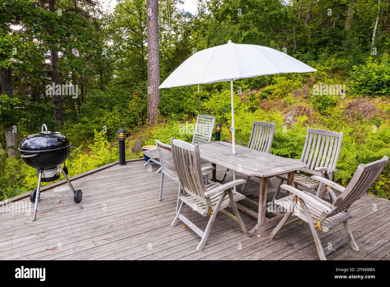 View of wooden patio of typical wooden Swedish house with table, barbecue,  chairs and sitting area with umbrella. Sweden. Europe Stock Photo - Alamy