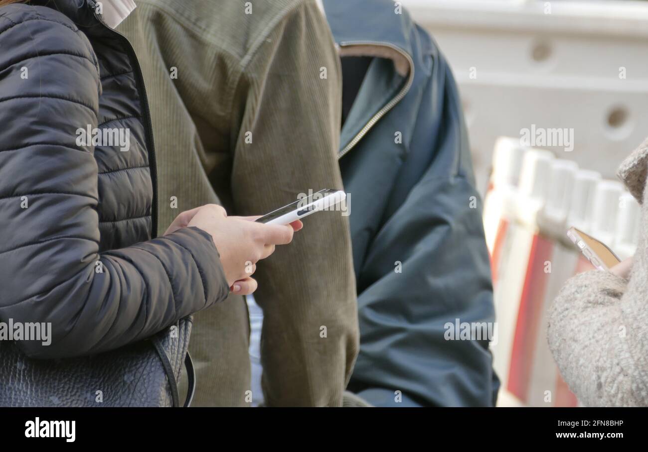 Hand holding smartphone, person reading smartphone news.  Woman standing in line for appointed shopping. Stock Photo
