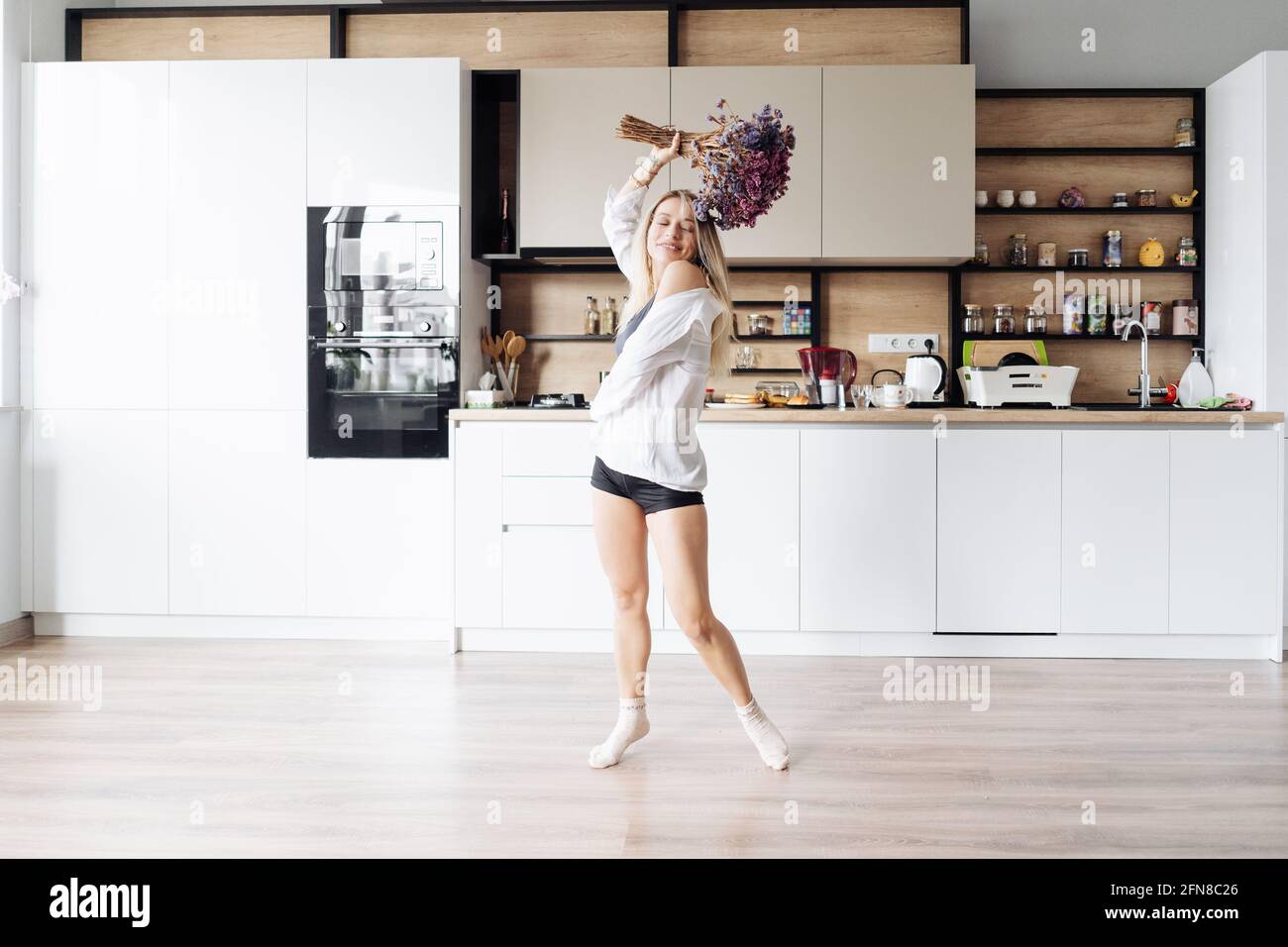 Happy young woman dancing alone in kitchen showing carefree lifestyle and independence