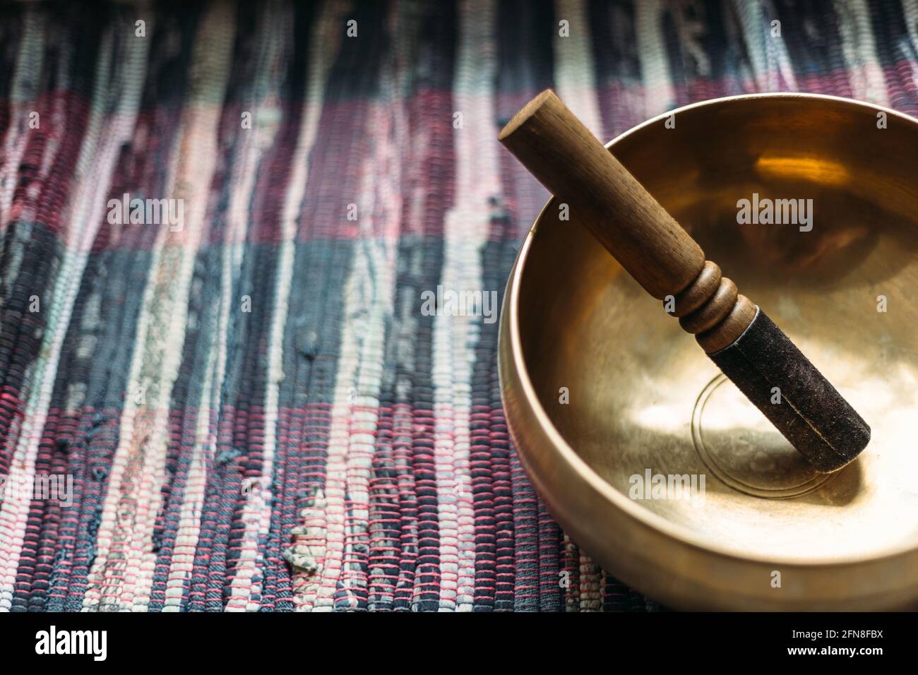 Tibetan singing bowl with a stick on a handmade woven carpet. Stock Photo