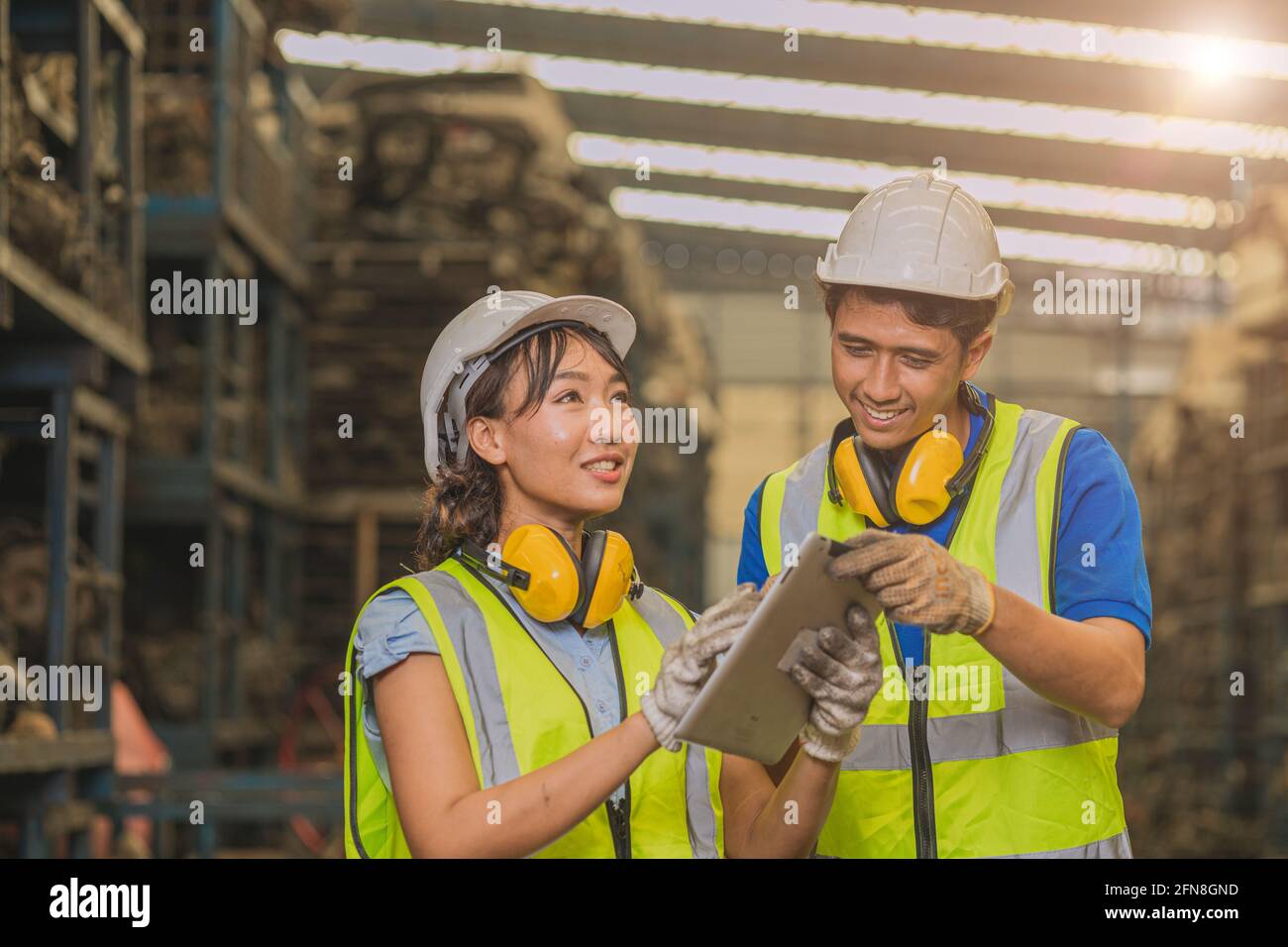 Asian young man and women worker team engineer working help support together using tablet happy smile to work in factory industry. Stock Photo