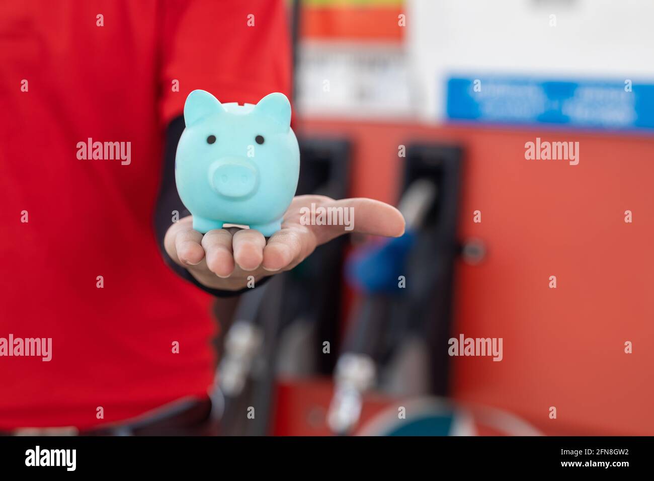 Gas station staff worker with piggy bank for save money from low fuel price, gas costs reduction, cut and saving gasoline drop price concept. Stock Photo