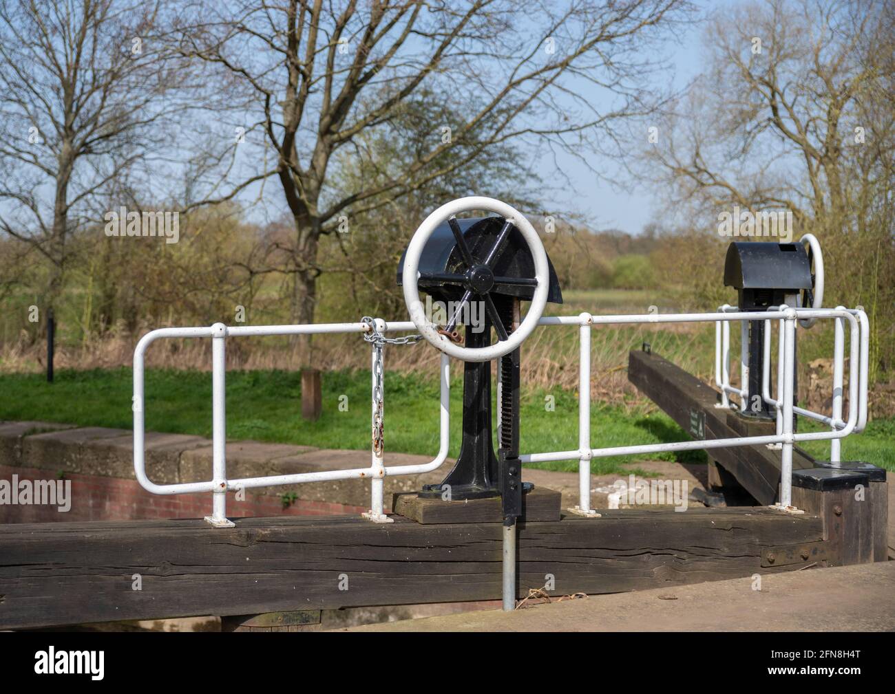Canal lock gate with paddle crank wheel and metal railing on wooden gate balance beam. Stock Photo