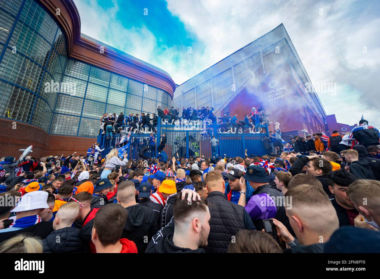 Glasgow, Scotland, UK. 15 May 2021. Thousands of supporters and fans of Rangers football club descend on Ibrox Park in Glasgow to celebrate winning the Scottish Premiership championship for the 55th time and the first time for 10 years. Smoke bombs and fireworks are being let off by fans tightly controlled by police away from the stadium entrances. Pic; Fans celebrate after full time at the gates of Ibriox. Iain Masterton/Alamy Live News Stock Photo