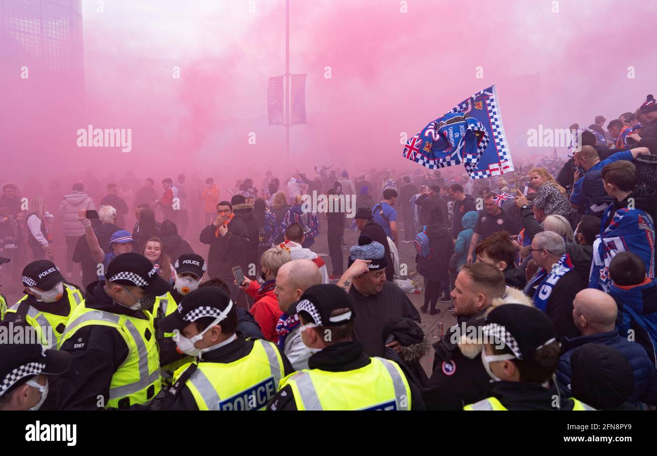 Glasgow, Scotland, UK. 15 May 2021. Thousands of supporters and fans of Rangers football club descend on Ibrox Park in Glasgow to celebrate winning the Scottish Premiership championship for the 55th time and the first time for 10 years. Smoke bombs and fireworks are being let off by fans tightly controlled by police away from the stadium entrances. Pic; Fans celebrate after full time at the gates of Ibriox. Iain Masterton/Alamy Live News Stock Photo