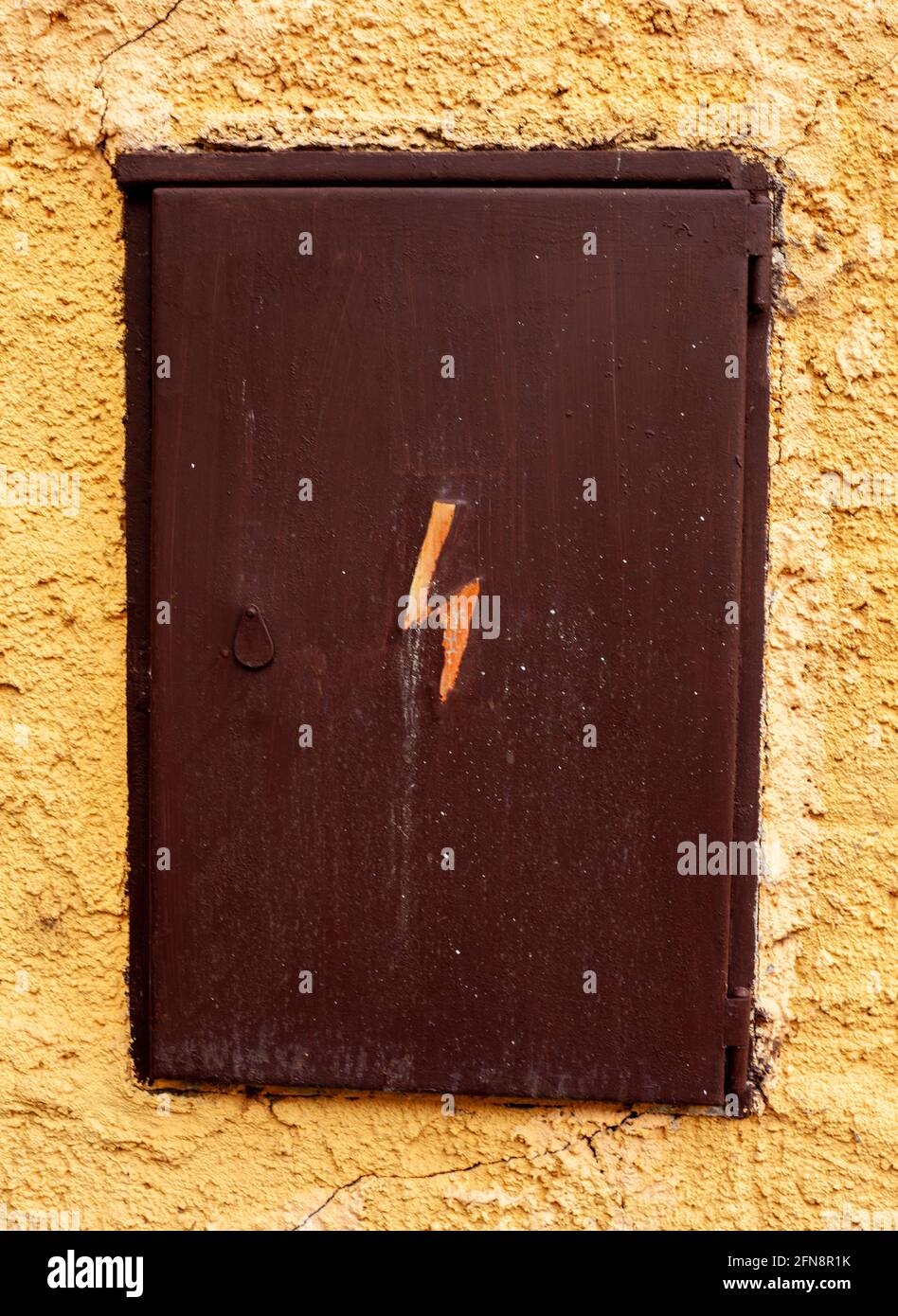An old outside electric box with the symbol of electricity, in a yellow wall. Stock Photo