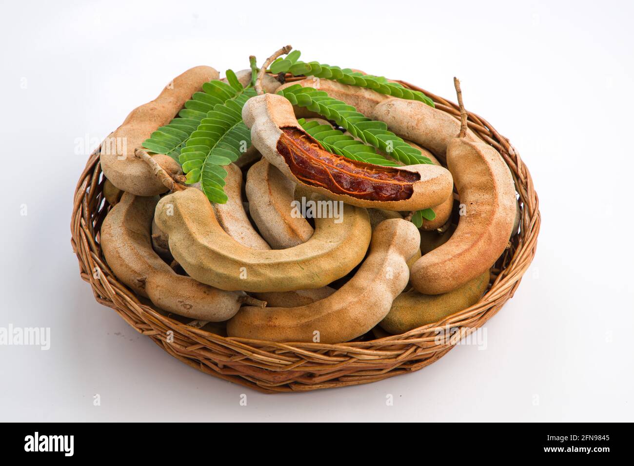 Tamarind  bean like pods filled with seeds surrounded by a fibrous pulp arranged in a basket with white textured background. Stock Photo