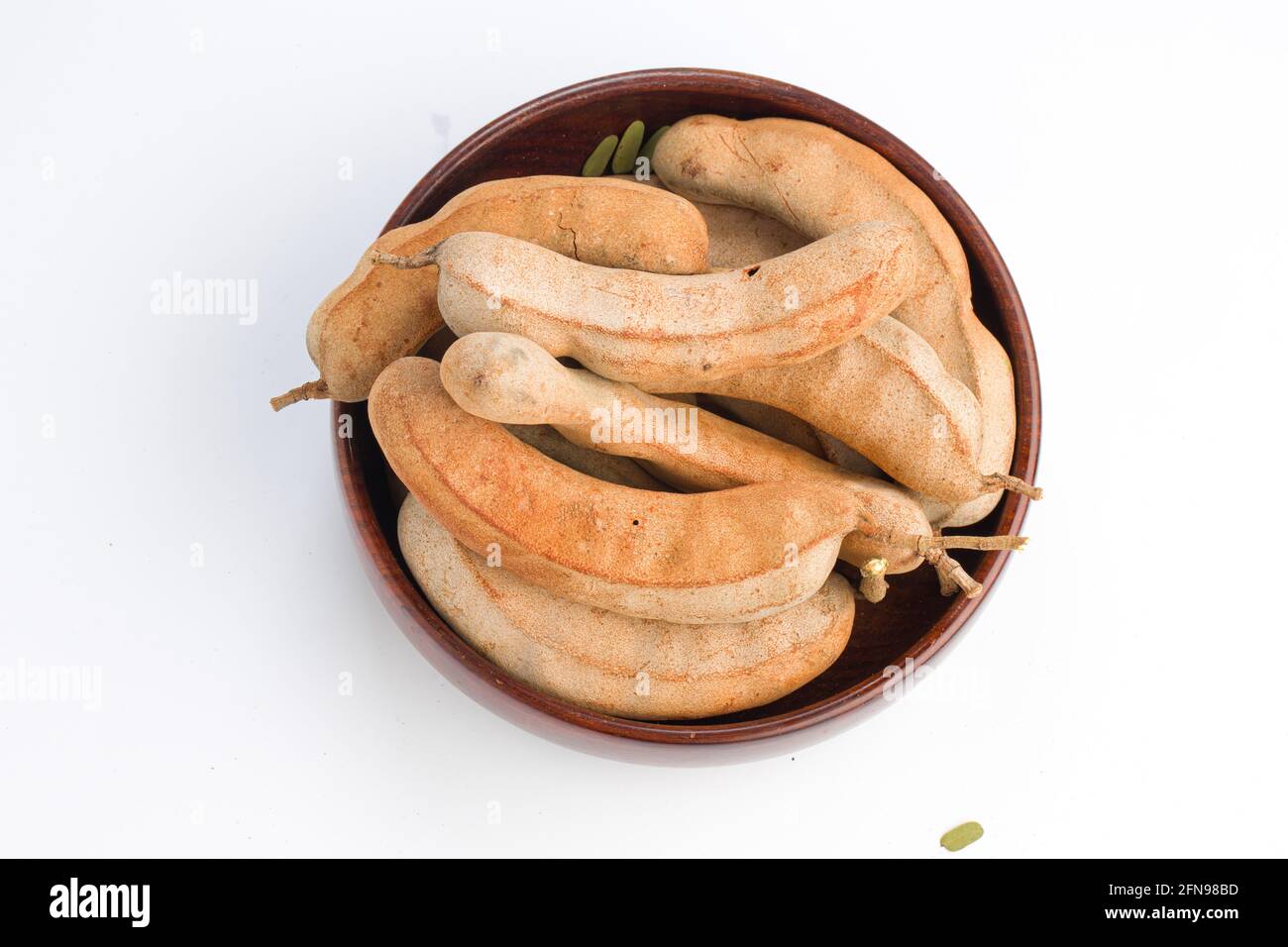 Tamarind  bean like pods filled with seeds surrounded by a fibrous pulp arranged in a basket with white textured background. Stock Photo