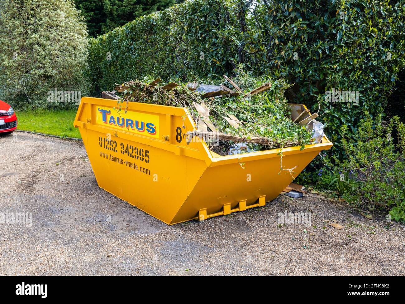 A large 8 yard overfilled yellow skip used for garden clearance and debris removal, full of garden waste in a drive in Surrey, south-east England Stock Photo
