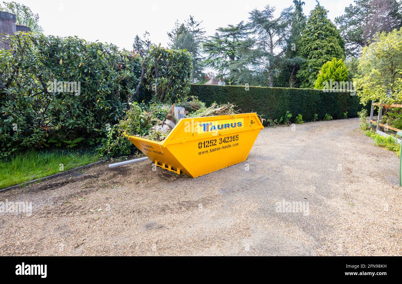 A large 8 yard overfilled yellow skip used for garden clearance and debris removal, full of garden waste in a drive in Surrey, south-east England Stock Photo