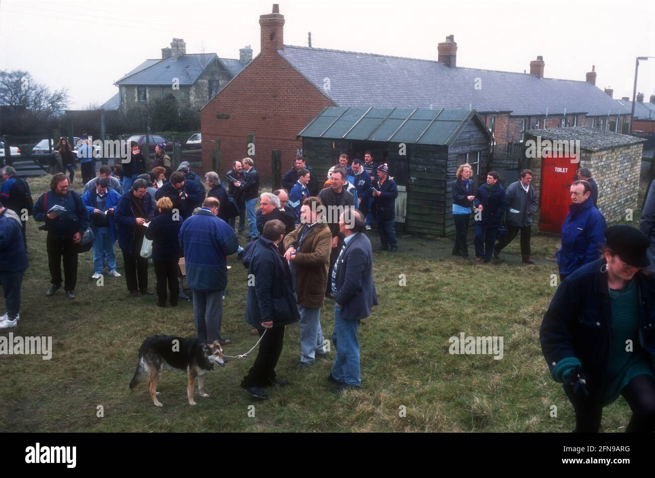A crowd of non-league football supporters reading match program and waiting to enter football ground before a game Stock Photo