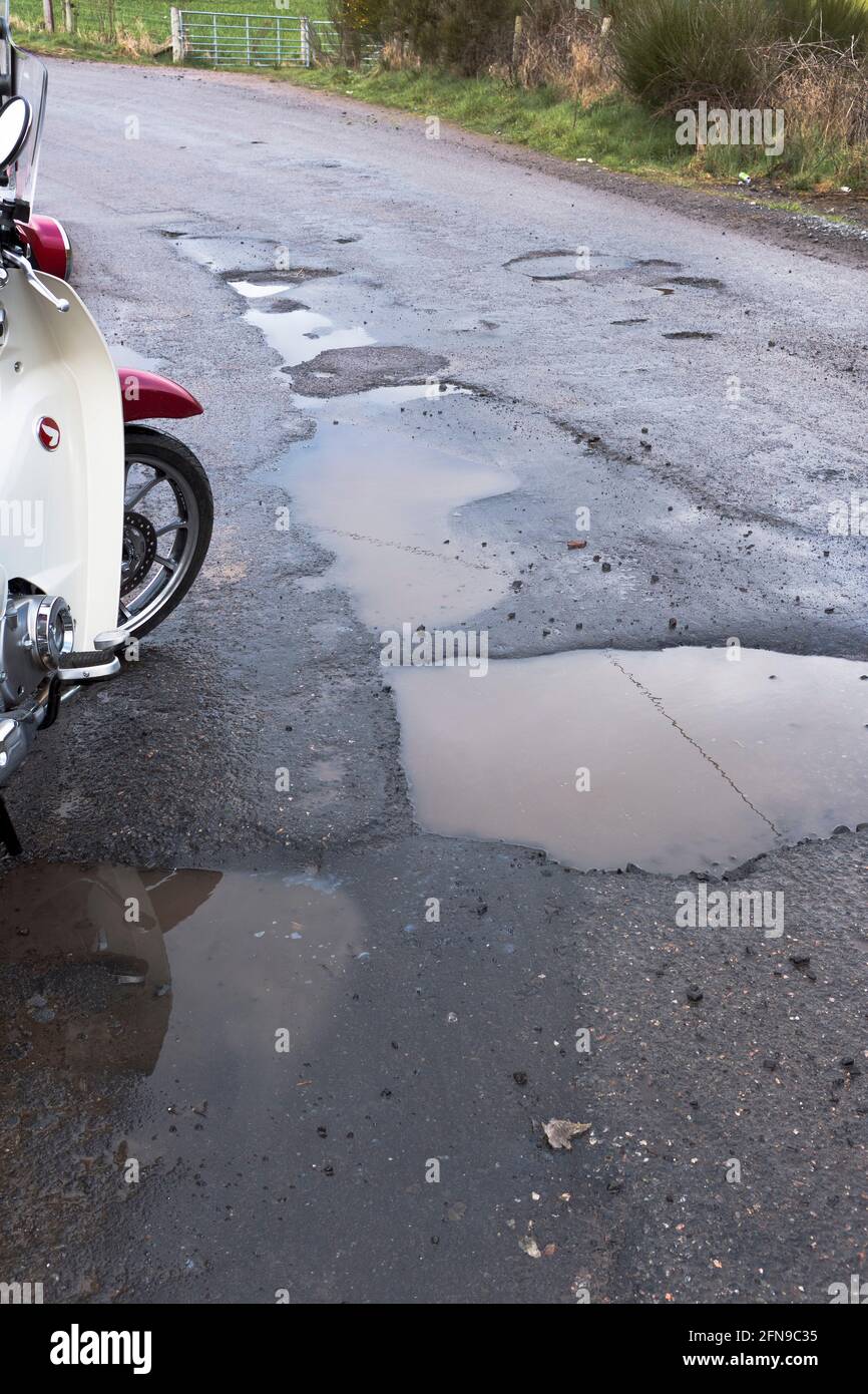 dh Roads SCOTLAND UK Pothole motorcycle by potholes deep puddle hole in damaged poor road surface Covid 19 winter weather damage repair close up Stock Photo