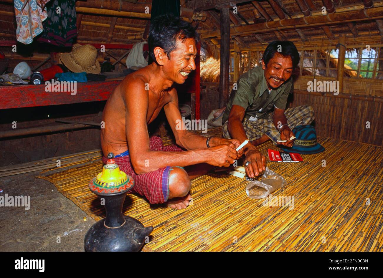 Malaysia/Borneo: Two Iban Headhunters sitting in the long house in the rain forest of Sarawak and preparing a pipe to smoke wheat Stock Photo