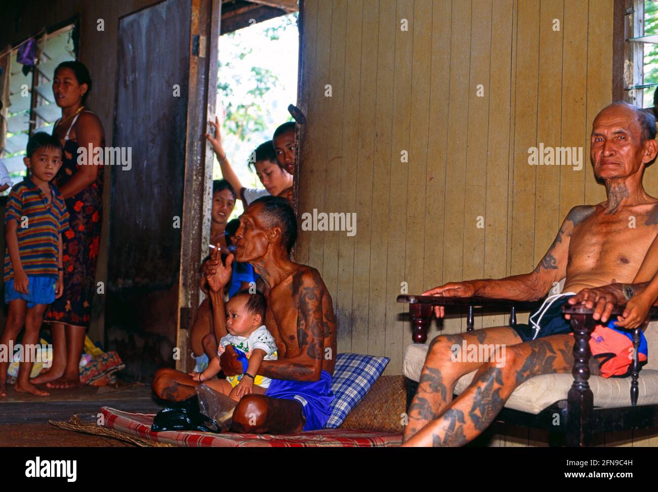 Malaysia/Borneo: Older Iban Headhunter sitting in a typical long house with lot's of kids around Stock Photo