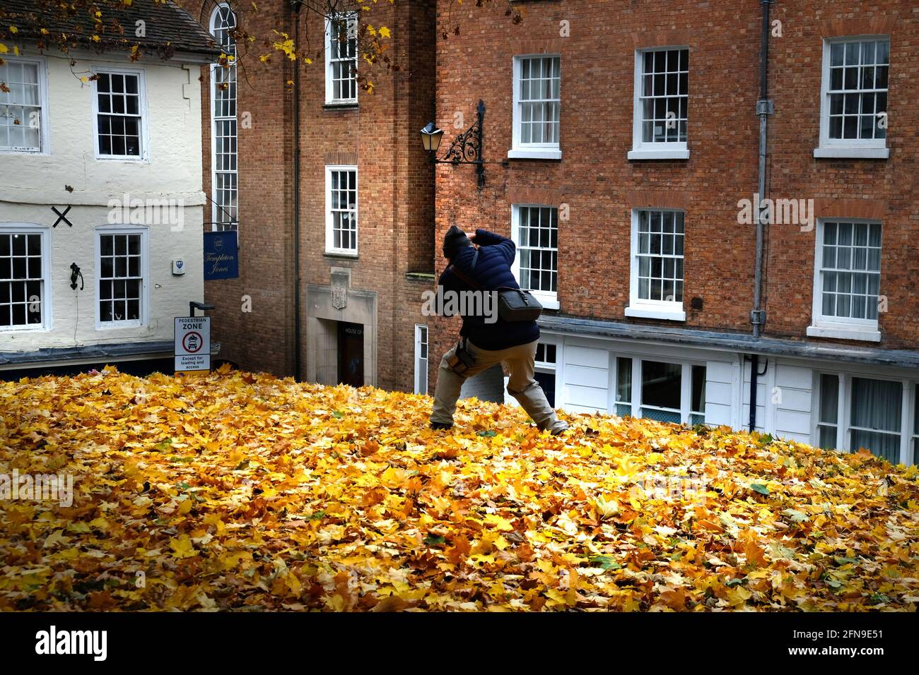 A male photographer raises a camera to compose a photograph in the churchyard of Old St Chad's, Shrewsbury, Shropshire, He compses a picture of the corner of College Hill and Princess Street Stock Photo