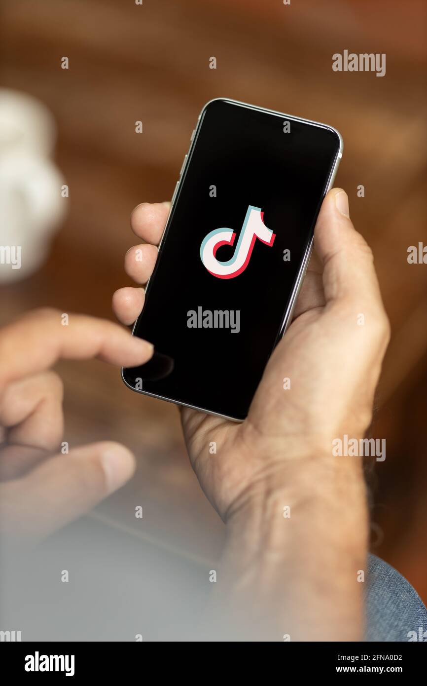 Man holding a smartphone in a cafe. TikTok logo on the display. Selective focus. Stock Photo