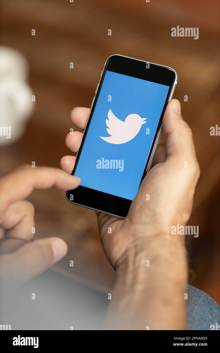 Man holding a smartphone in a cafe. Twitter logo on the display. Selective focus. Stock Photo