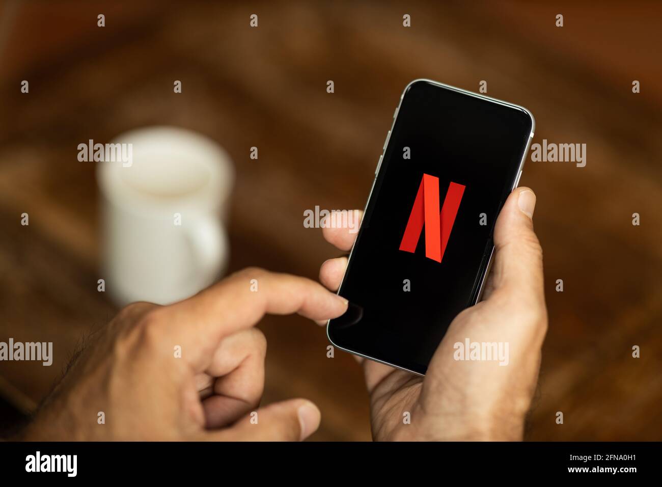 Man holding a smartphone in a cafe. Netflix logo on the display. Selective focus. Stock Photo