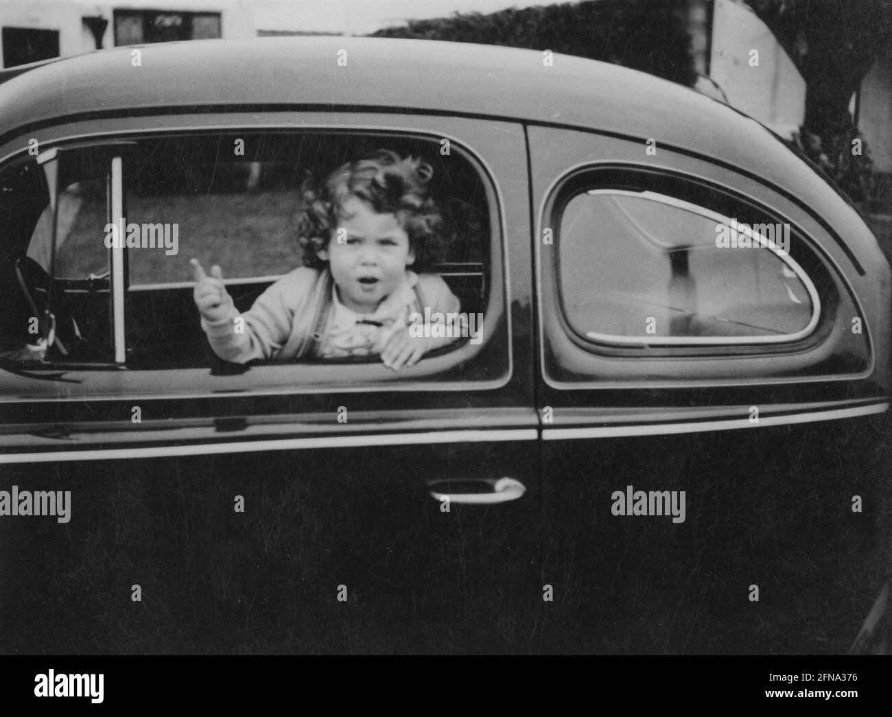 The little girl inside vintage car points through an open window in Santa Monica, CA 1941 - black and white stock photo Stock Photo