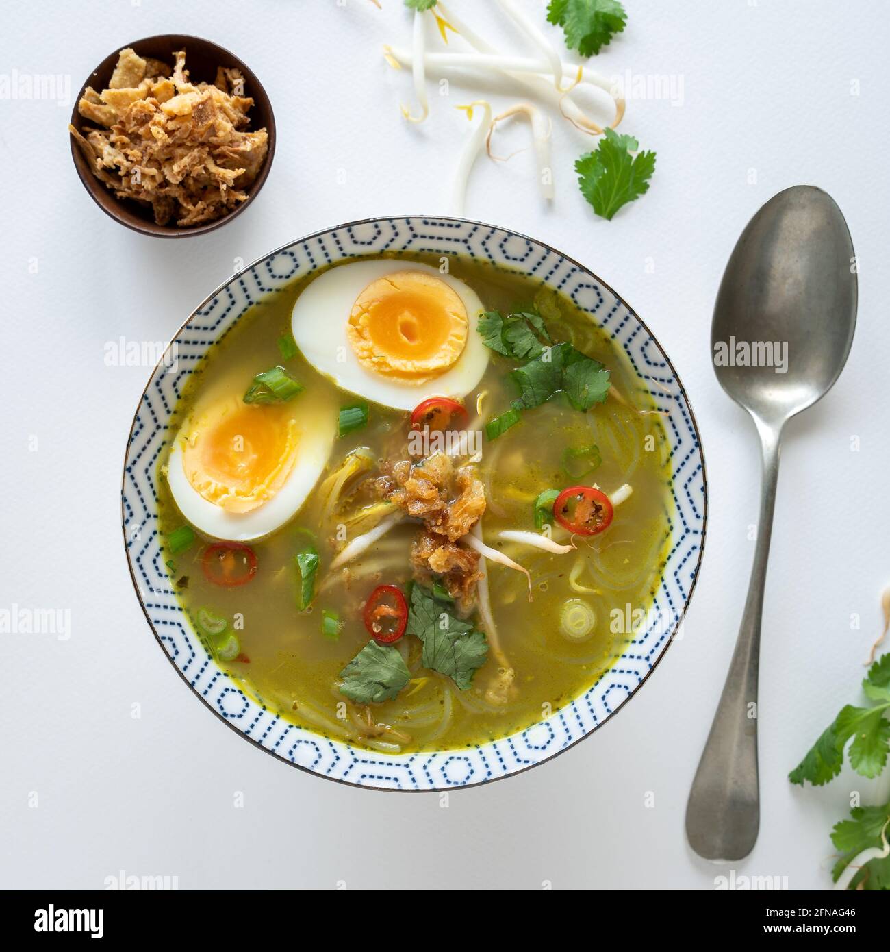 Flat-lay of a vegetarian Indonesian soup, traditionally made with chicken called soto ayam on white background with boiled egg and fried onions, copy Stock Photo