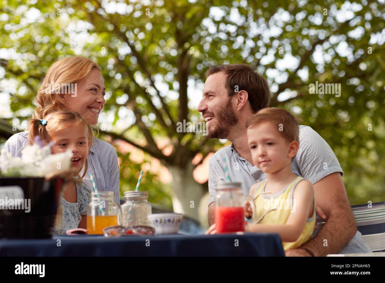 happy caucasian parents looking each other, smiling, with their children in laps, sitting outdoor Stock Photo