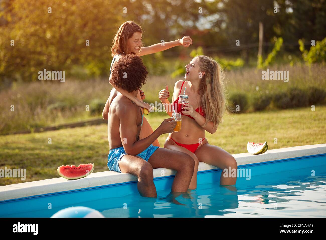 one afro-american young man having fun with two caucasian women by the pool Stock Photo