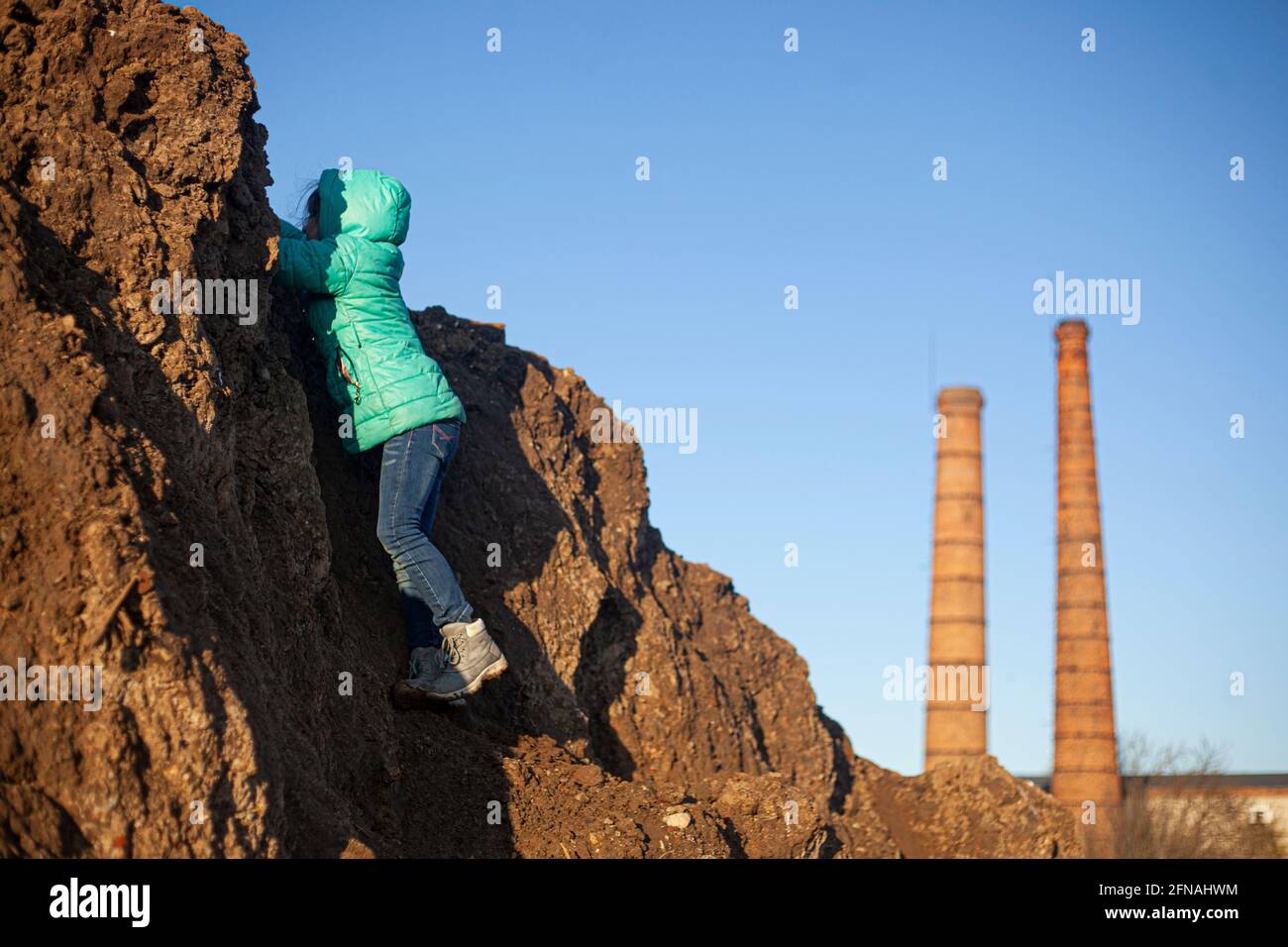 A girl is climbing a mountain. The child is dirty clothes. Child at the construction site. Big mountain of the earth. The lost girl is looking for a w Stock Photo