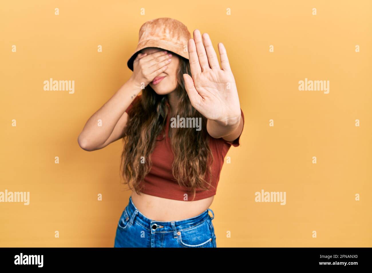 Young hispanic girl wearing casual clothes and hat covering eyes with hands and doing stop gesture with sad and fear expression. embarrassed and negat Stock Photo
