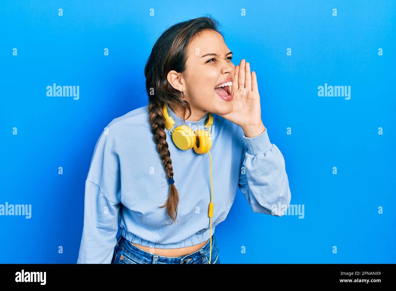 Young hispanic girl listening to music using headphones shouting and