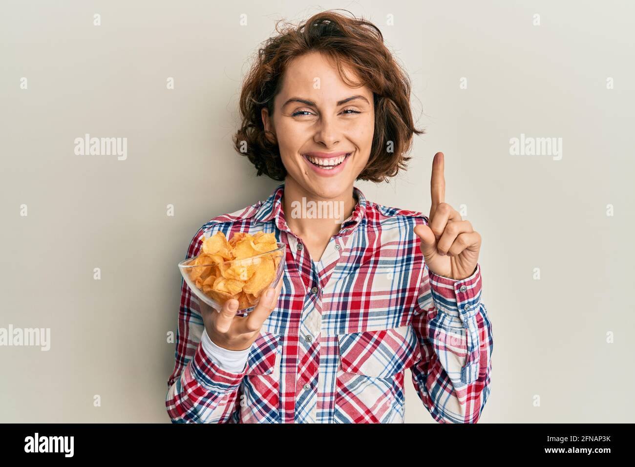Young woman holding potato chips smiling with an idea or