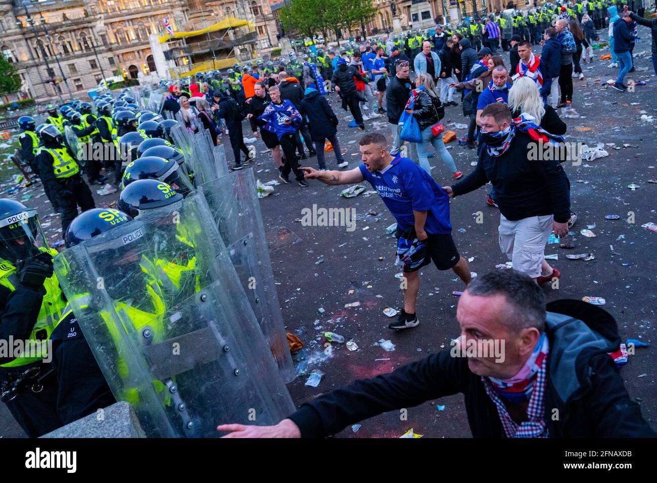 Glasgow, Scotland, UK. 15 May 202. Rangers football supporters  celebrating 55th league victory are cleared from George Square by police in riot gear on Saturday evening. In very violent scenes police were pelted with bottles and items from a nearby construction site as police pushed the supporters into the south west corner of the square. Pic; Police are confronted by angry Rangers fans. Iain Masterton/Alamy Live News. Stock Photo