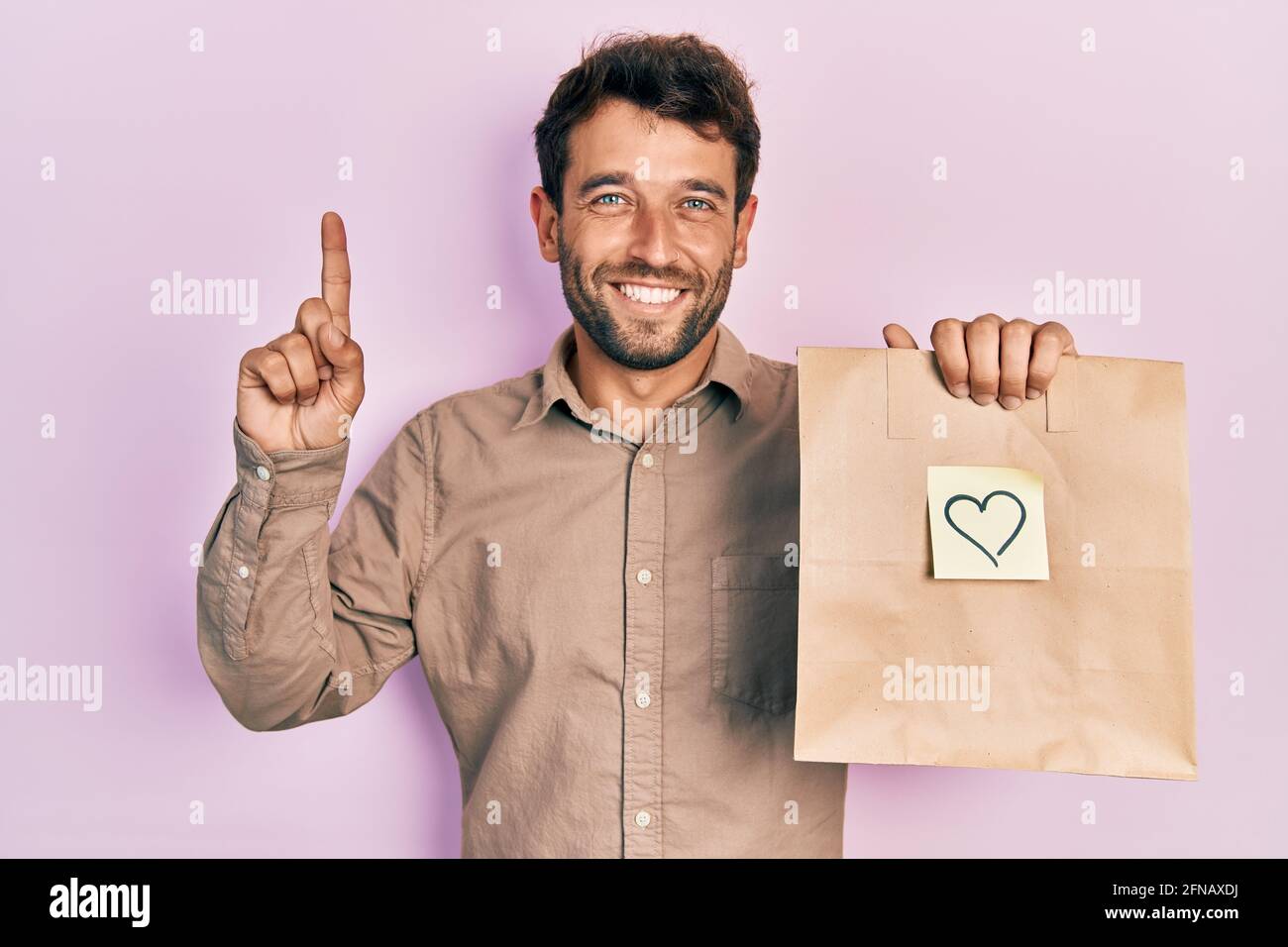 Handsome Man With Beard Holding Delivery Paper Bag With Heart Reminder Smiling Amazed And 2996