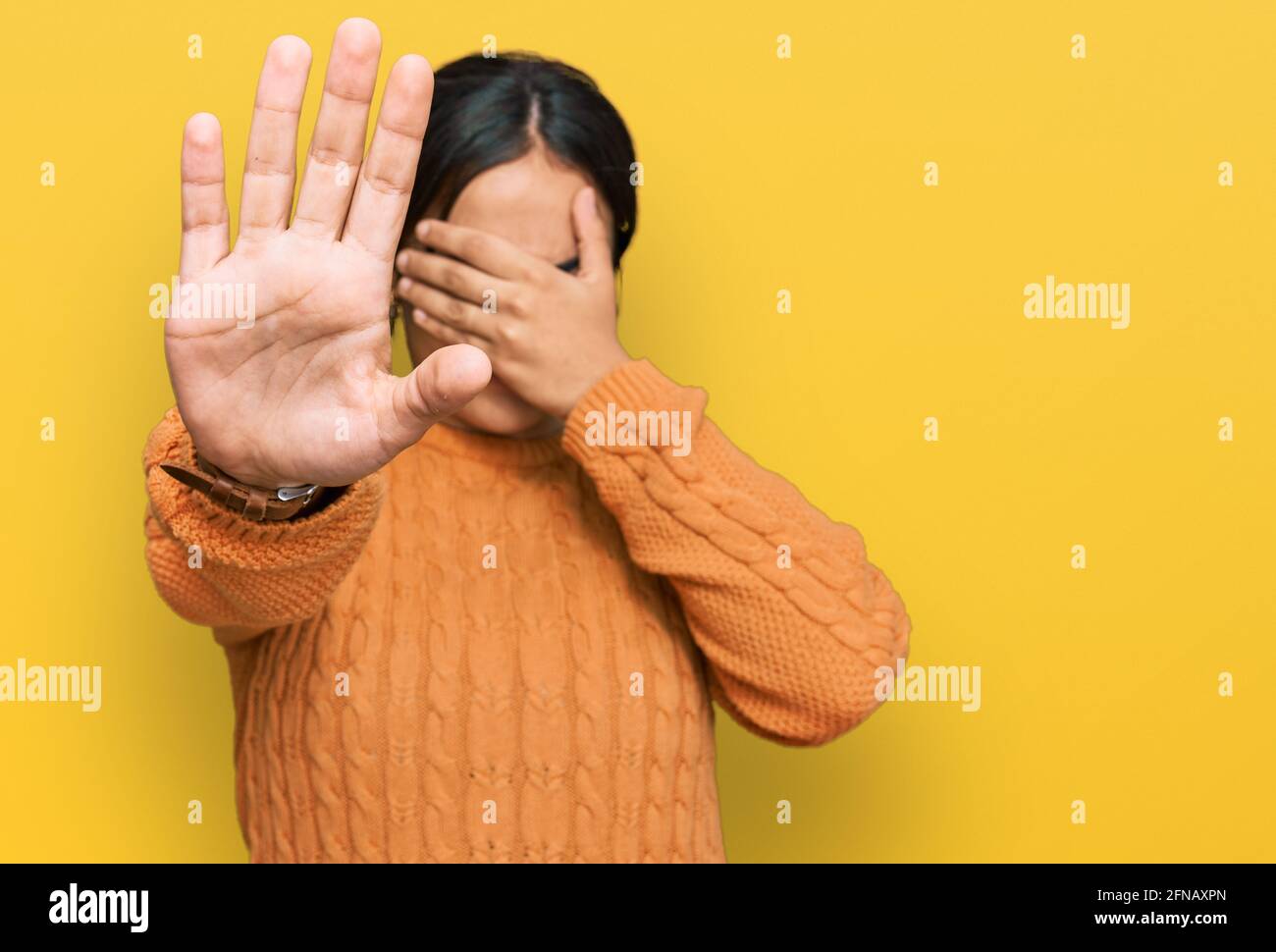 Young brunette woman wearing casual winter sweater covering eyes with hands and doing stop gesture with sad and fear expression. embarrassed and negat Stock Photo