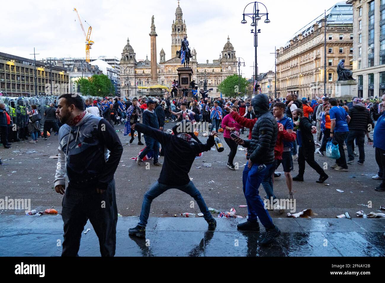 Glasgow, Scotland, UK. 15 May 202. Rangers football supporters  celebrating 55th league victory are cleared from George Square by police in riot gear on Saturday evening. In very violent scenes police were pelted with bottles and items from a nearby construction site as police pushed the supporters into the south west corner of the square. Pic; Man throws bottle towards police line.  Iain Masterton/Alamy Live News. Stock Photo