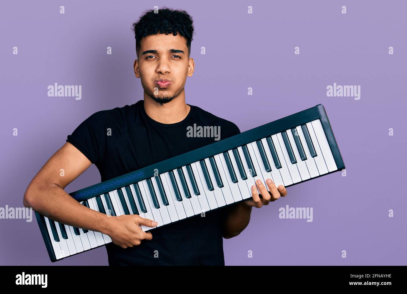 Young african american man holding piano keyboard puffing cheeks with funny  face. mouth inflated with air, catching air Stock Photo - Alamy
