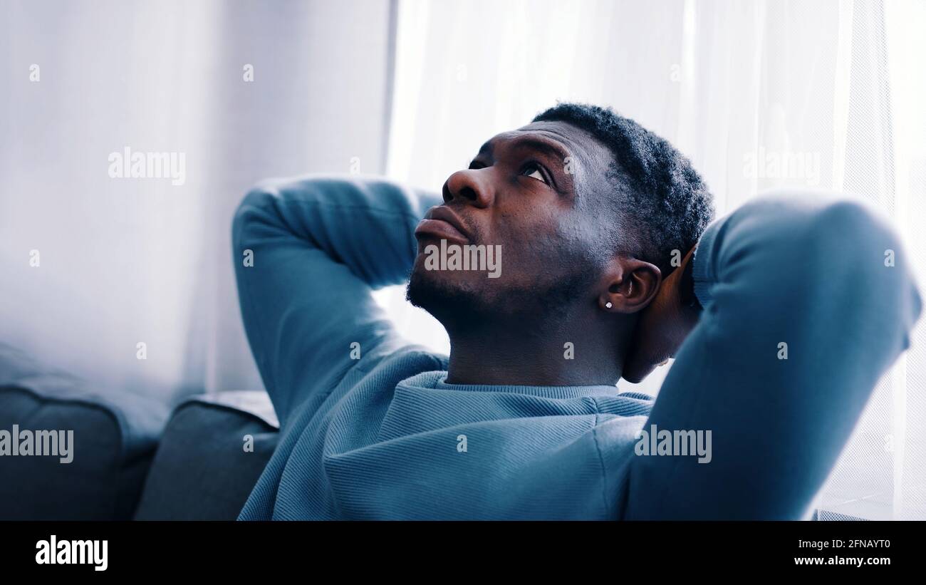 Serious man thinking while sitting on a blue sofa - Hands behind the ...