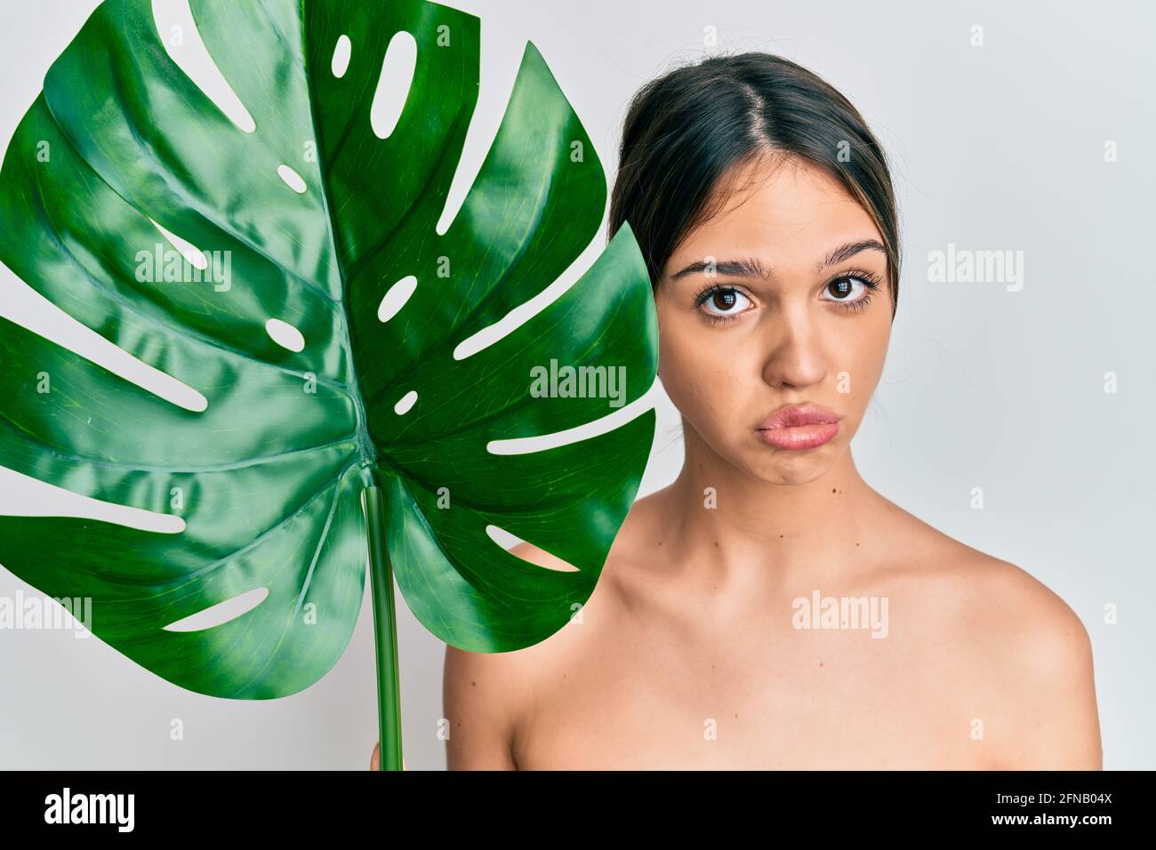Young brunette woman holding green plant leaf close to beautiful face depressed and worry for distress, crying angry and afraid. sad expression. Stock Photo