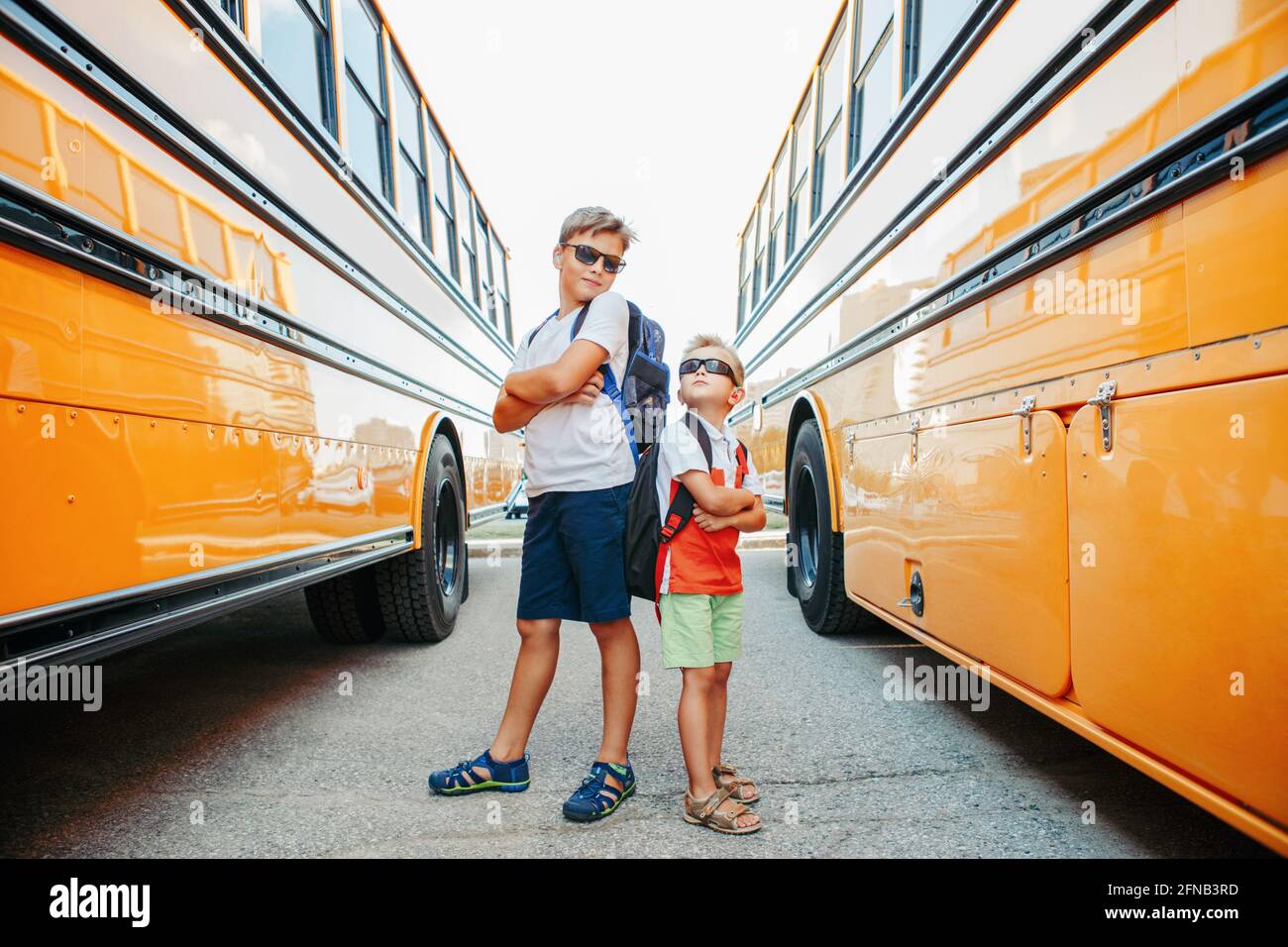 Back to school. Caucasian brothers students standing by yellow school bus. Cool kids in sunglasses going back to school in September. Educational syst Stock Photo