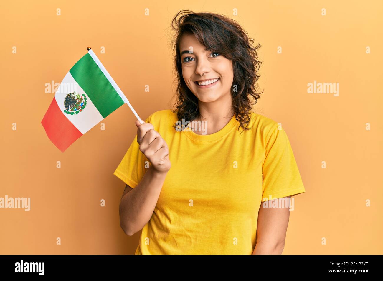 Young hispanic woman holding mexico flag looking positive and happy