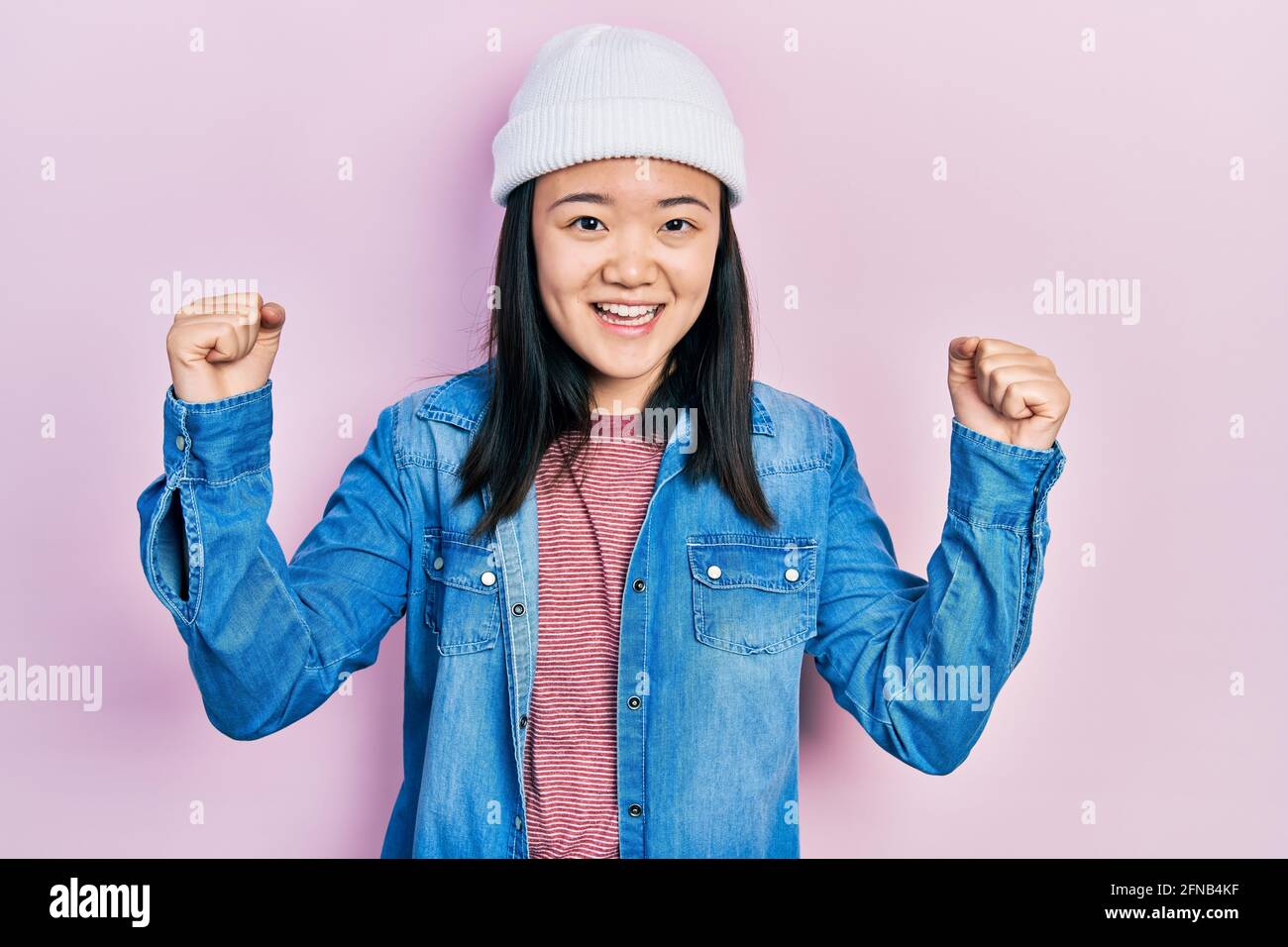 Young chinese girl wearing cute wool cap screaming proud, celebrating victory and success very excited with raised arms Stock Photo