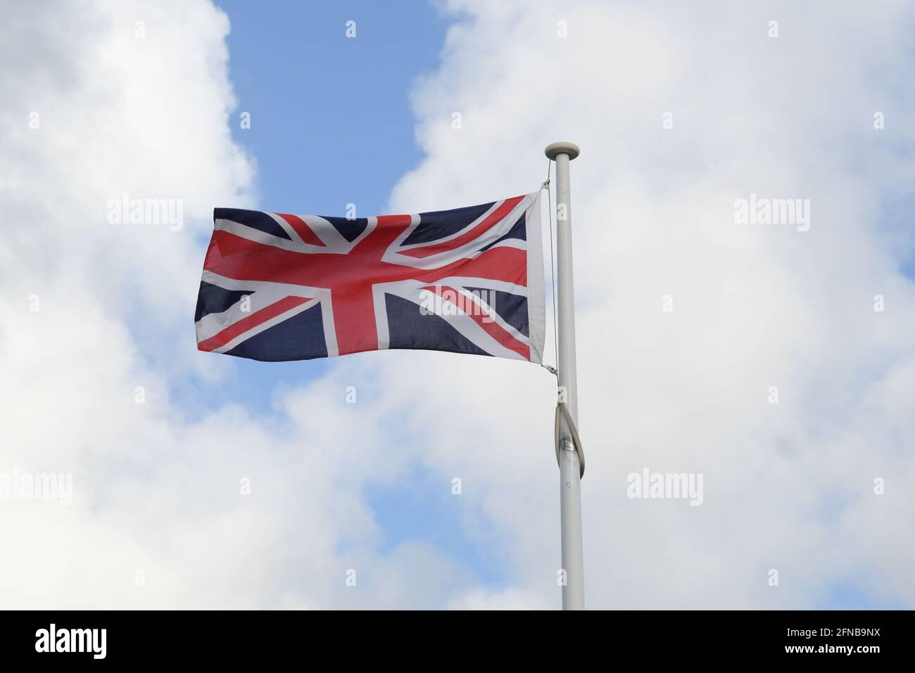 The Union Jack, or Union Flag, flying on a windy day, with bright blue sky and white clouds in the background Stock Photo