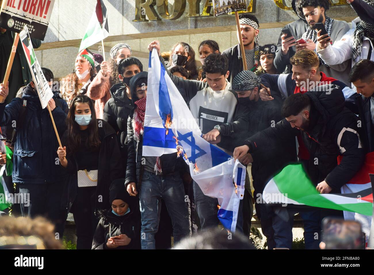 London, UK. 15th May, 2021. Protesters burn the Israeli flag outside the Royal Garden Hotel near the Embassy of Israel during the pro-Palestine protest. Thousands of people marched in London in support of Palestine. Credit: SOPA Images Limited/Alamy Live News Stock Photo