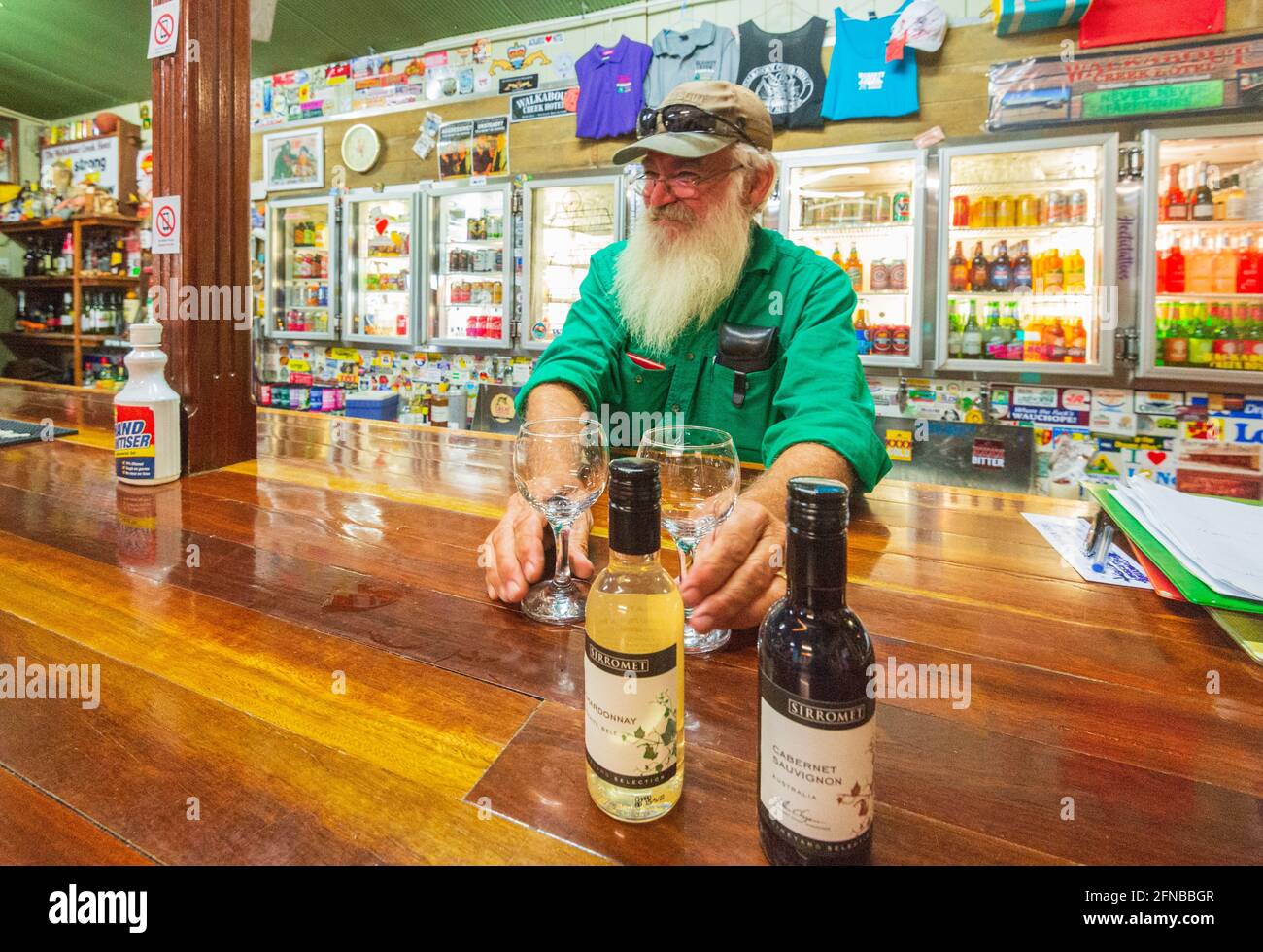 Smiling old bartender with a long white beard serving bottles of wine at the Walkabout Creek Hotel featured in the Crocodile Dundee's movie, Central Q Stock Photo
