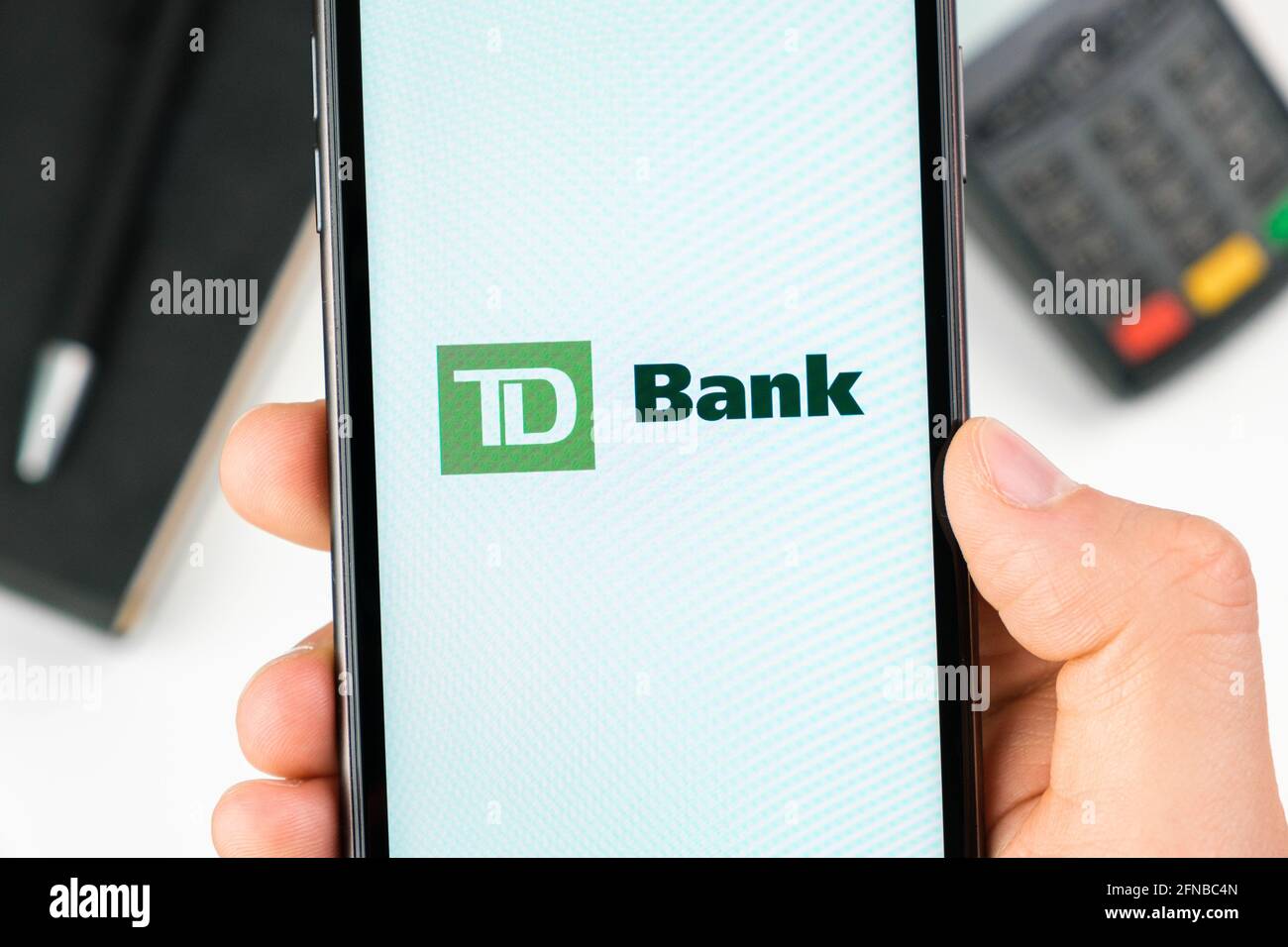 TD bank logo on the smartphone screen in mans hand on the background of payment terminal, May 2021, San Francisco, USA Stock Photo
