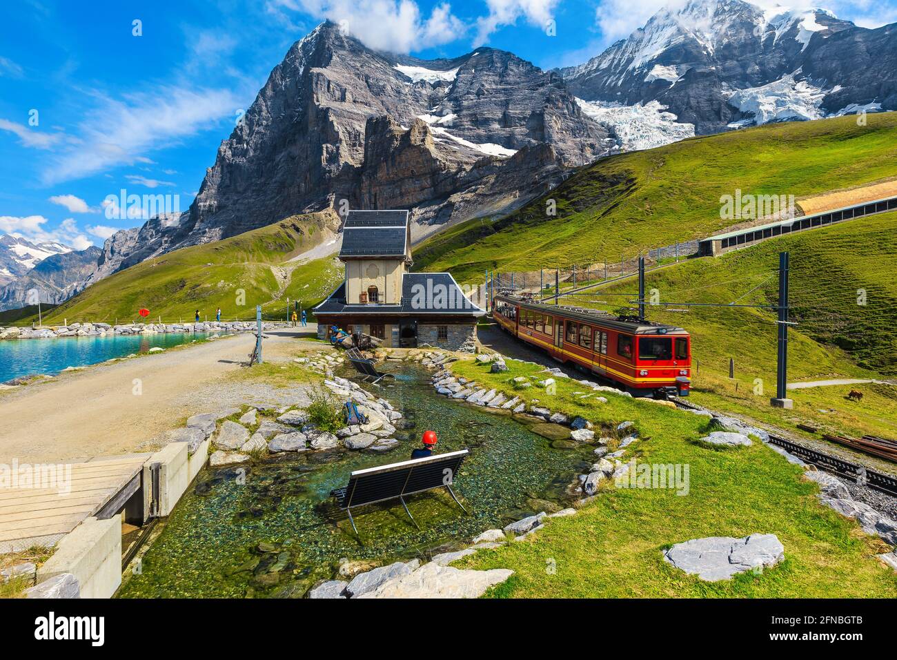 Cogwheel red passenger train in the small mountain station. Small train station on the shore of the Fallbodensee lake, Jungfraujoch, Bernese Oberland, Stock Photo