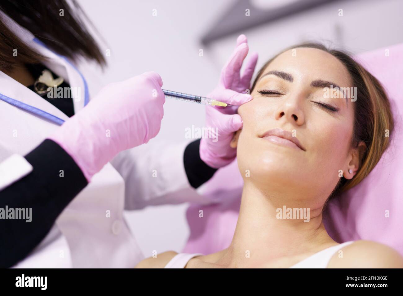 Doctor injecting hyaluronic acid into the cheekbones of a woman as a facial rejuvenation treatment. Stock Photo