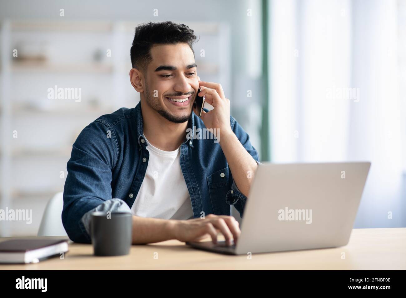 Successful middle-eastern guy talking on phone while working at home Stock Photo