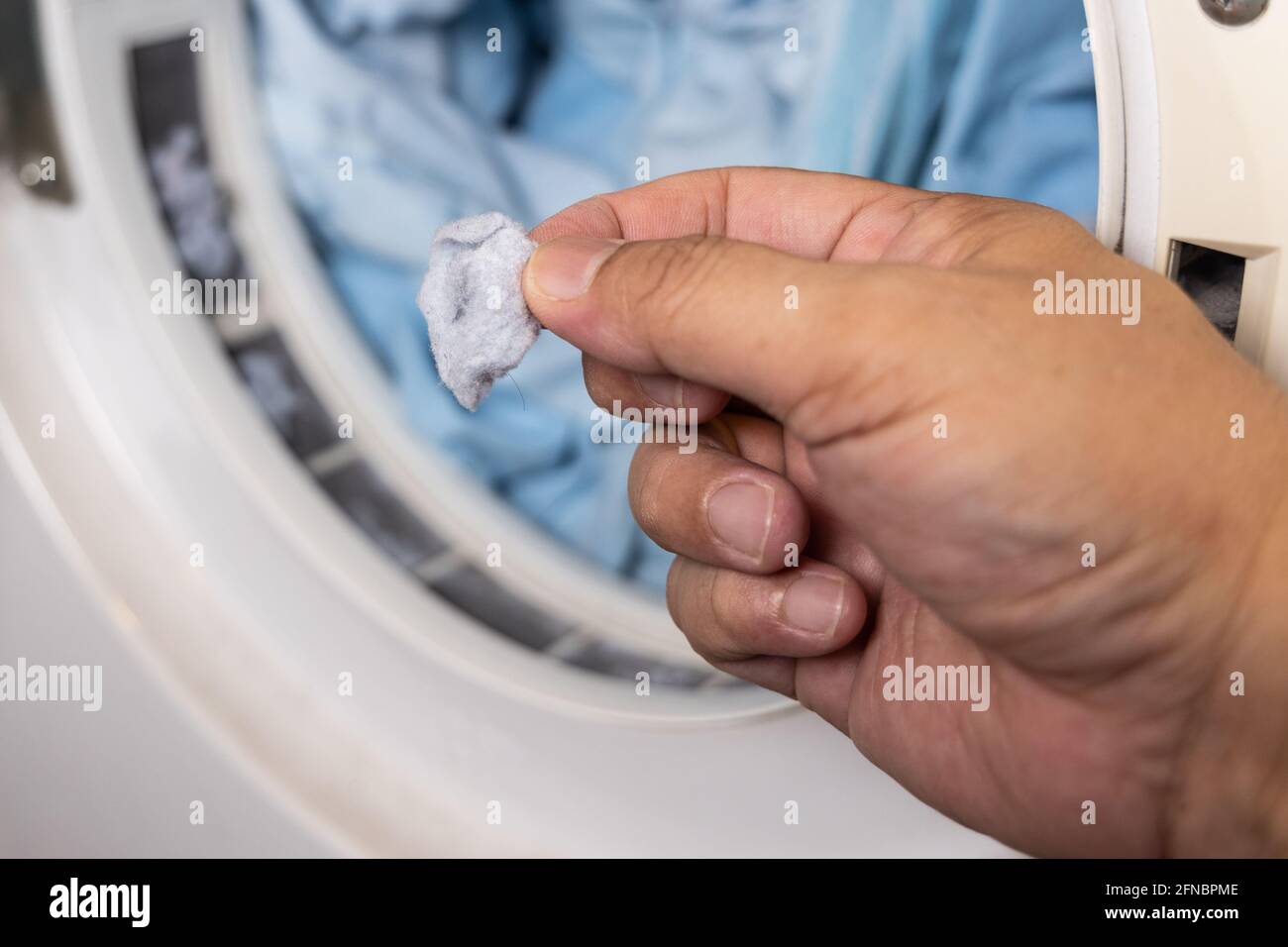 Hand removing lint from fabric trapped on laundry dryer filter Stock Photo