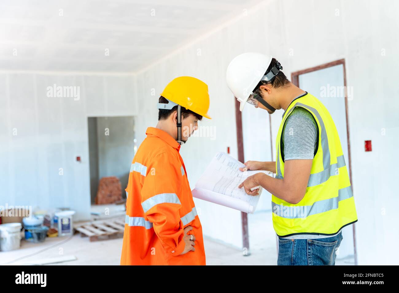 Asian architect and engineer fiving instructions to his foreman on clipboard working at construction site Stock Photo