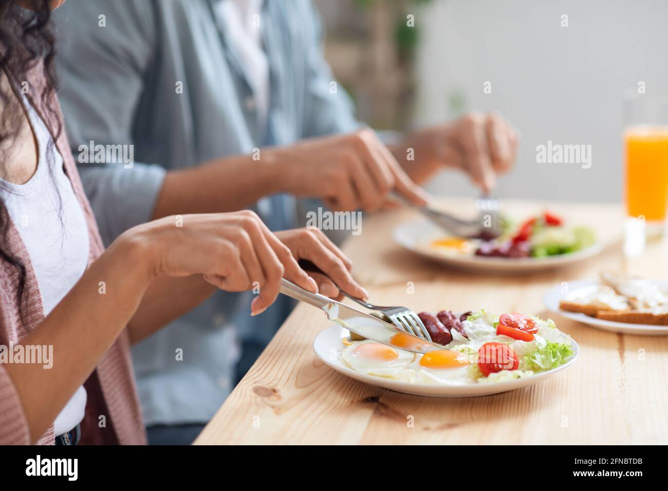 Unrecognizable couple using fork and knife while eating tasty breakfast